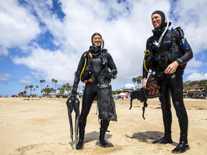 two divers in scuba gear talking on the beach